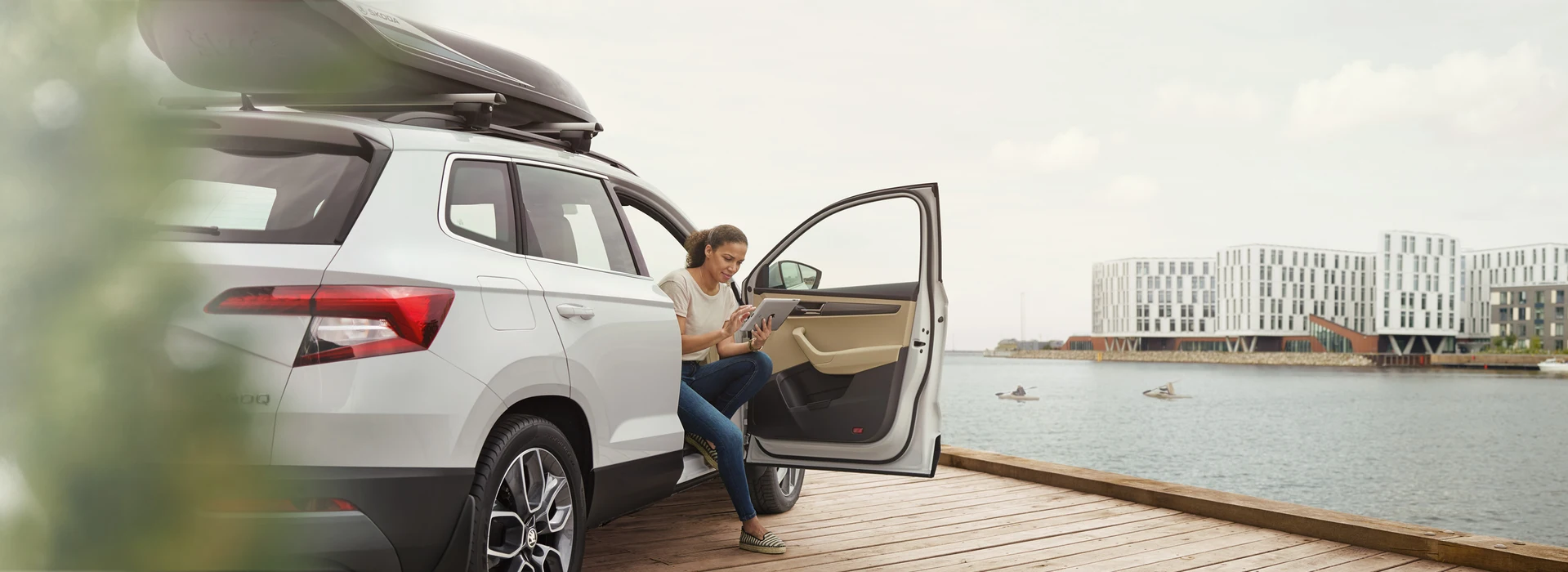 Frau sitzt am Hafen im geöffneten Škoda, nutzt Tablet bei geöffneter Tür.