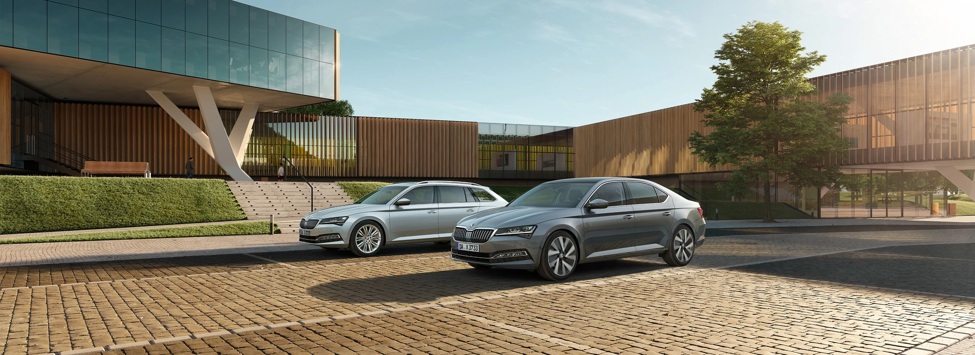 Zwei Škoda Superb Modelle vor moderner Glasfassade auf gepflastertem Vorplatz geparkt.