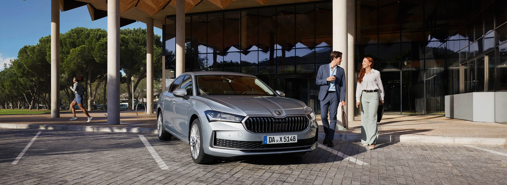 Eleganter Škoda vor Bürogebäude, Business-Paar geht am Auto vorbei.