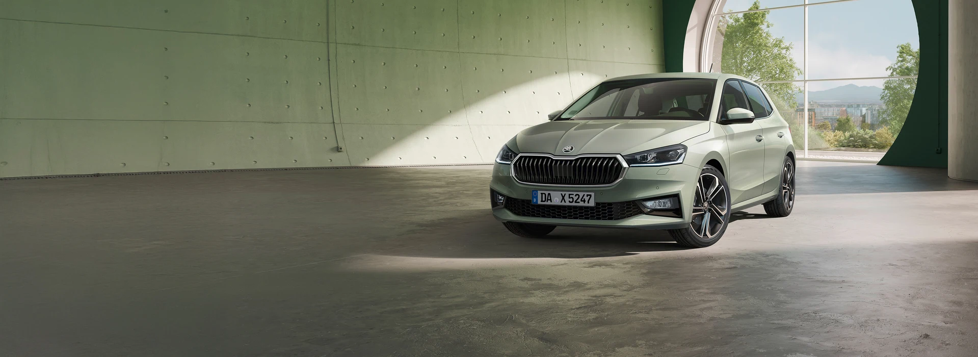 Frontansicht eines grünen Škoda Fabia, der in einem modernen Raum mit Betonwänden und natürlichem Licht steht.