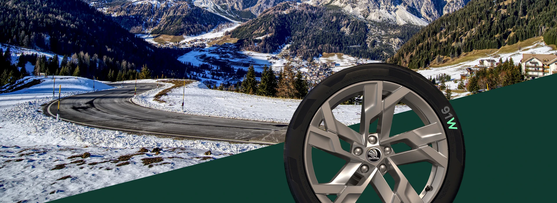 Schneebedeckte Berglandschaft mit einer kurvigen Straße und einem Škoda-Autoreifen im Vordergrund. Auf der Felge steht die Aufschrift ‚91W‘, wobei das W in Grün hervorgehoben ist.