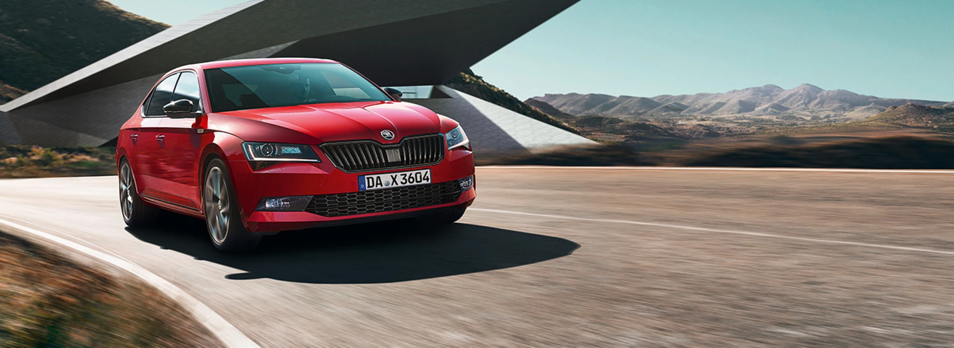 Ein roter Skoda fährt auf einer Straße unter einem modernen Betonbauwerk.
