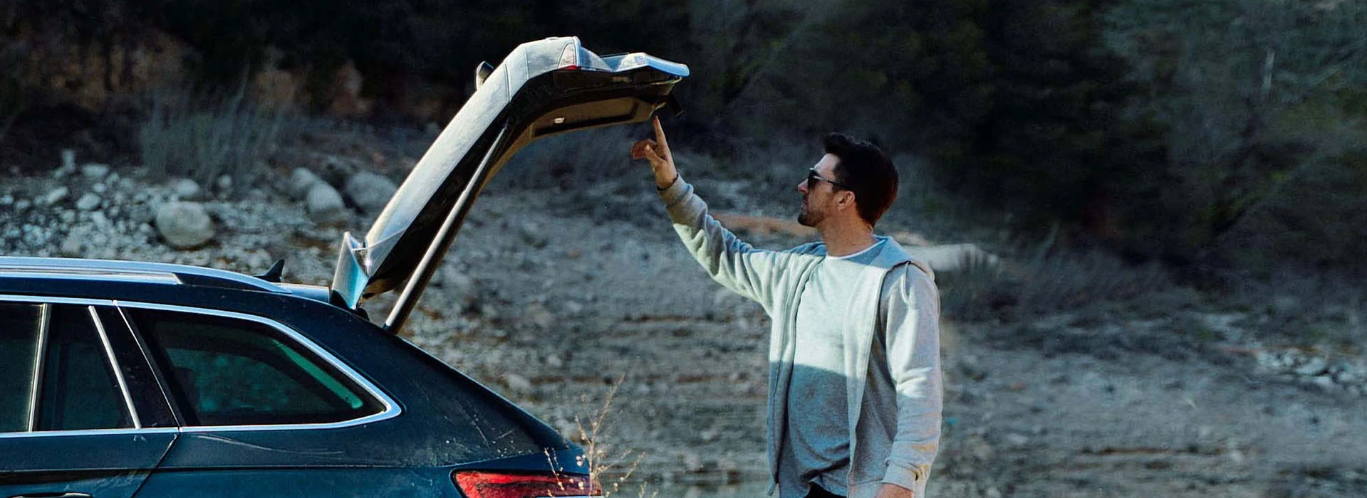 Mann schließt elektrisch öffnende Heckklappe eines Škoda Autos im Freien.