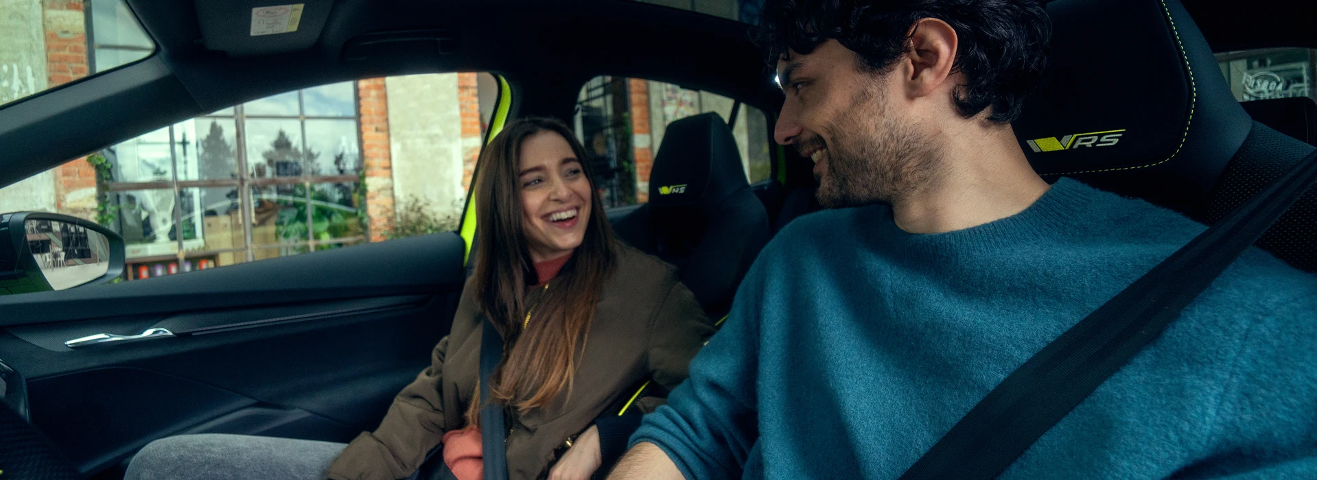 Zwei junge Erwachsene lachen gemeinsam auf Vordersitzen eines Škoda Modells.