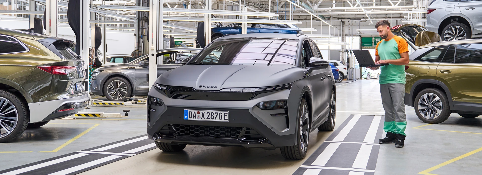 Mechaniker in Werkstatt prüft mit Laptop einen grauen Škoda Elroq in der Qualitätskontrolle.