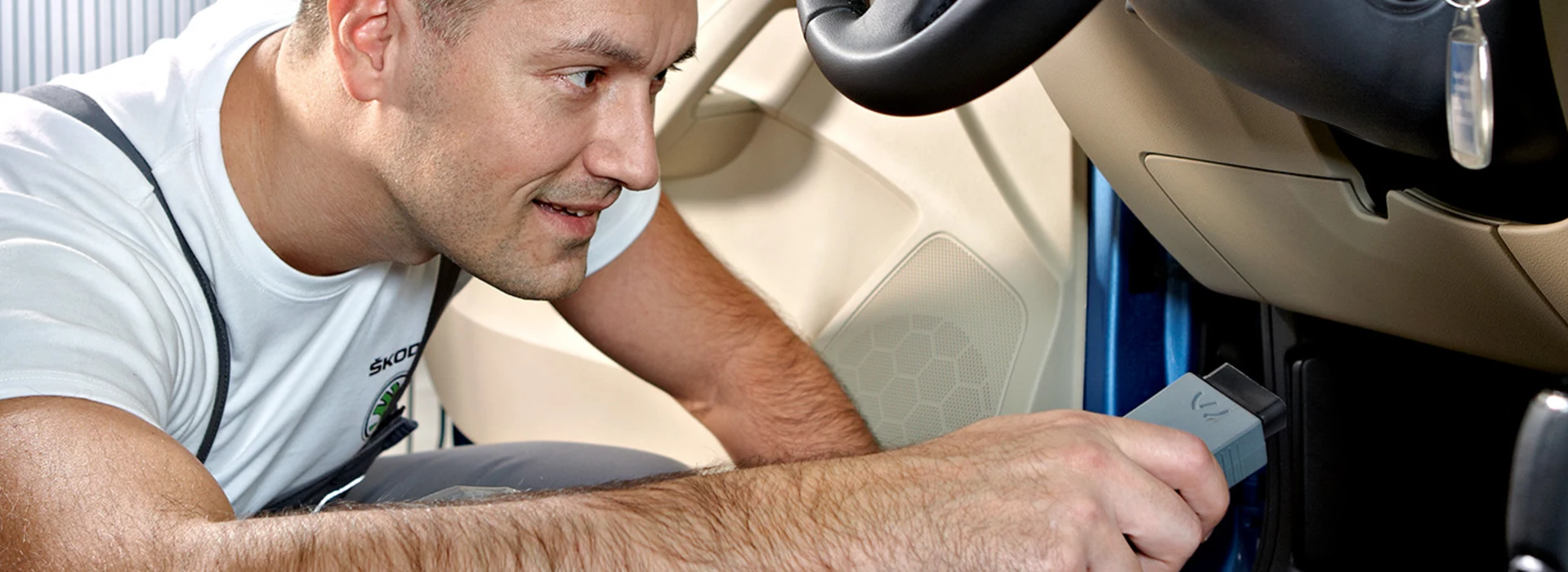 Škoda-Servicetechniker steckt Diagnosegerät in Anschluss unter dem Lenkrad eines Fahrzeugs.