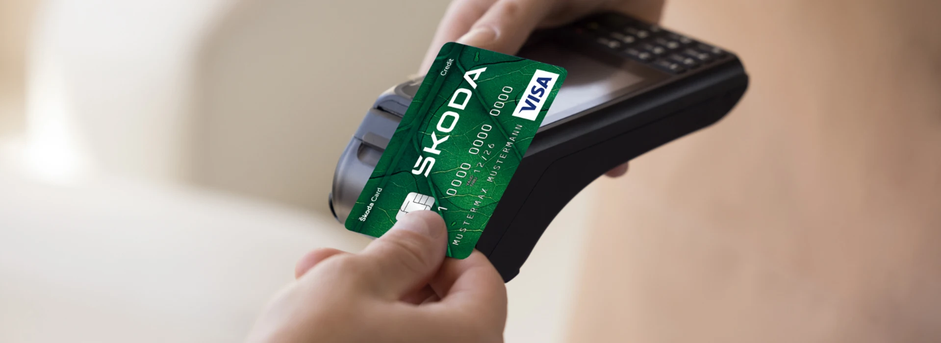 Nahaufnahme: Hand hält grüne Škoda Visa Karte an ein Kartenlesegerät – kontaktloses Bezahlen wird durchgeführt.