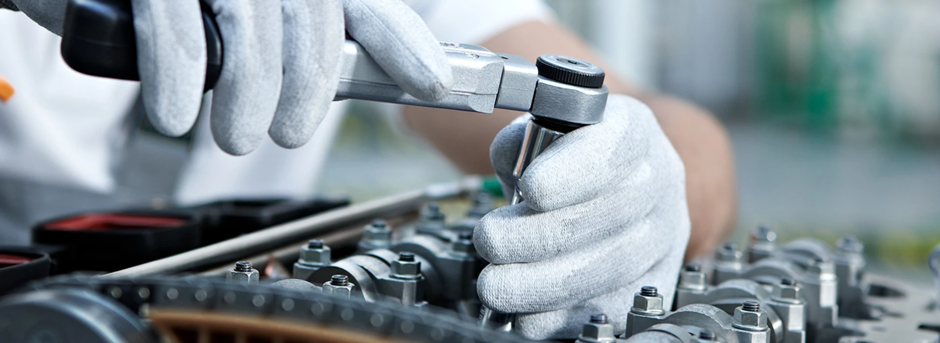 Ein Mechaniker mit weißen Handschuhen schraubt konzentriert an einem Motor.