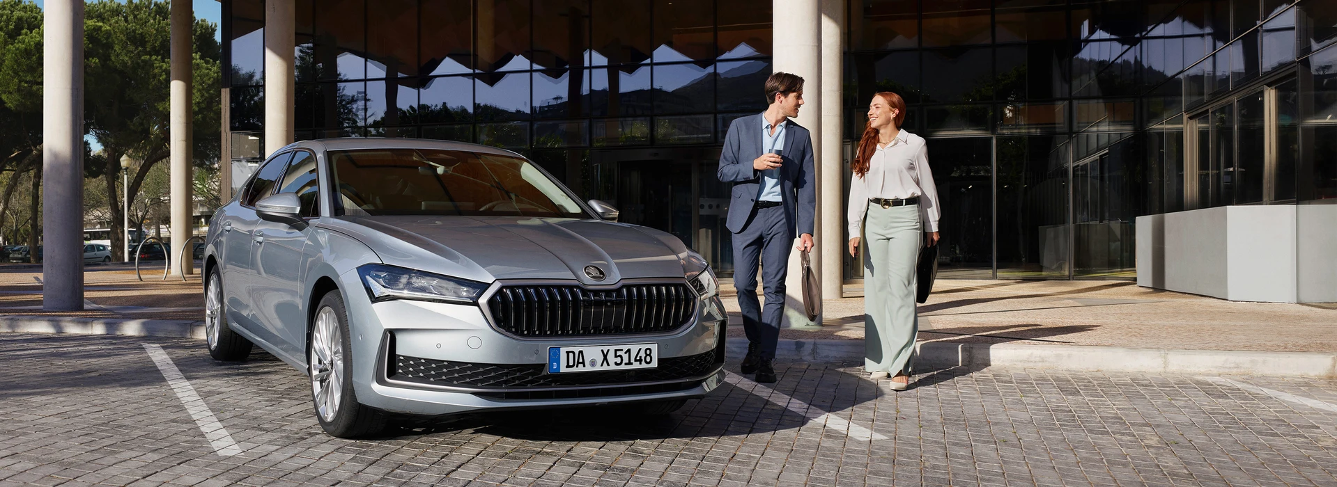 Geschäftsfrau und -mann laufen neben geparktem Škoda Superb