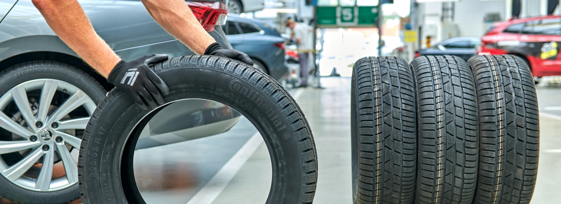 Mechaniker mit Handschuhen rollt Reifen vor mehreren anderen Reifen in Werkstatt