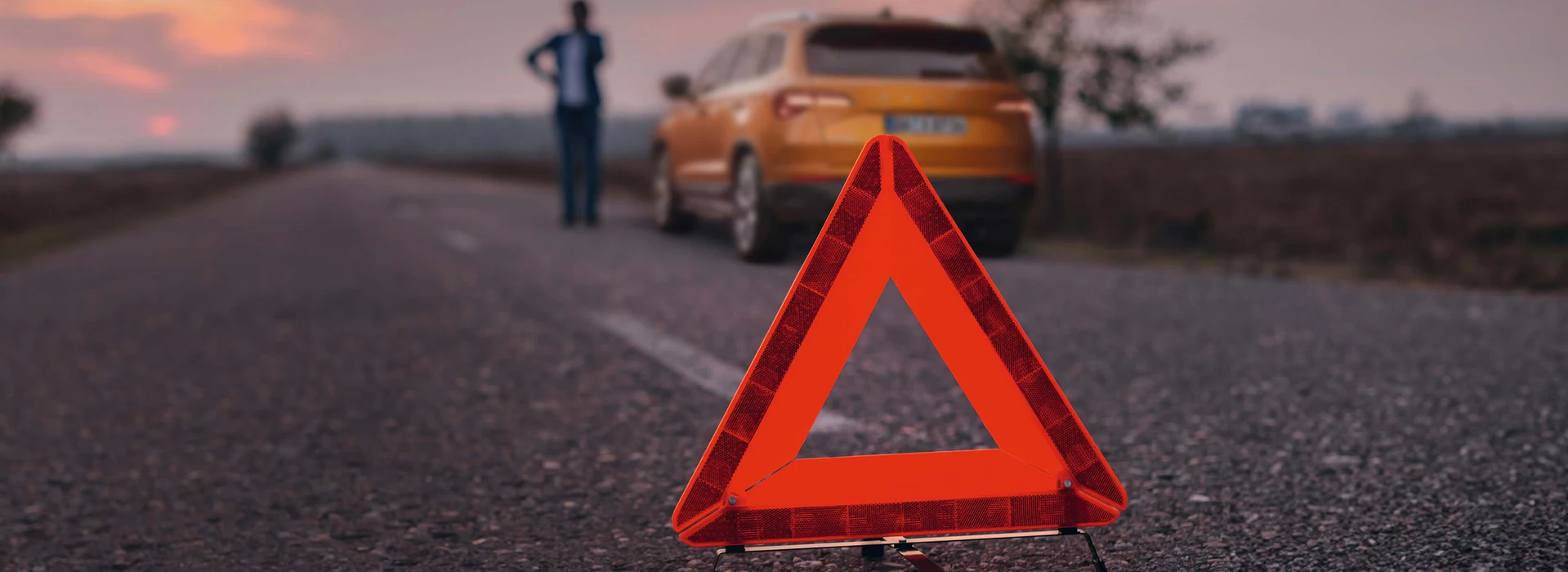 Warndreieck auf Landstraße bei Sonnenuntergang, Auto mit Person im Hintergrund.