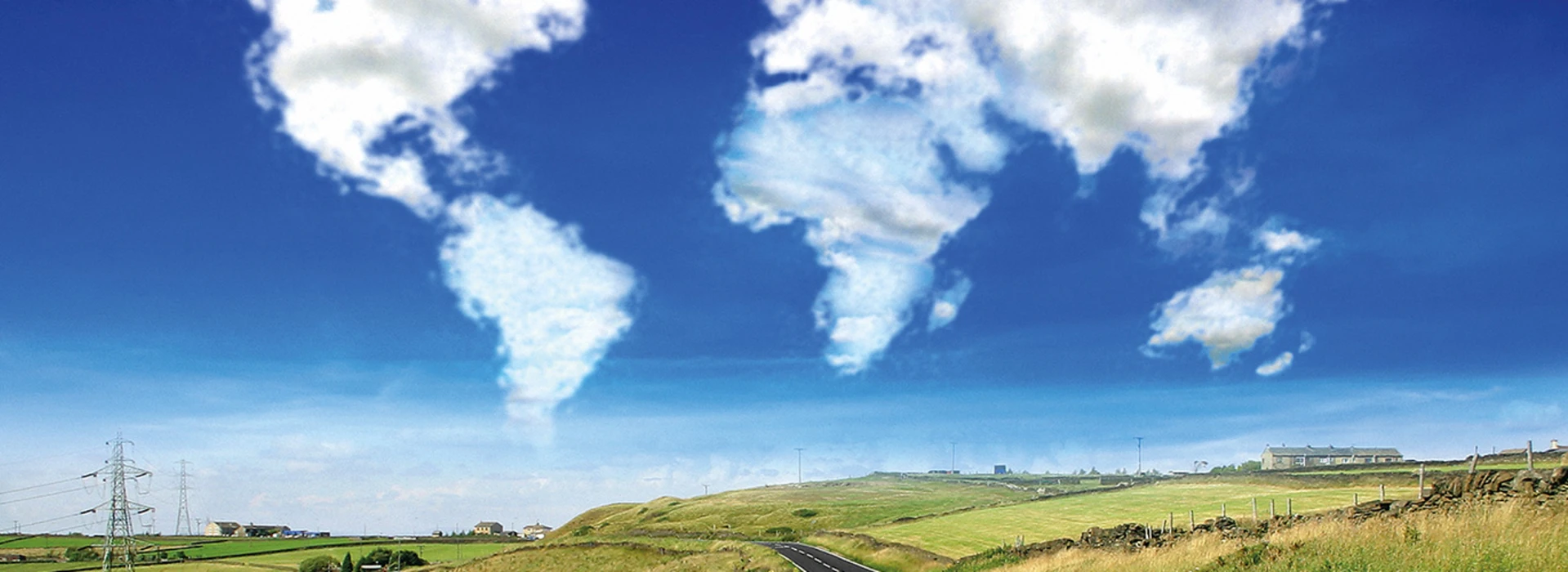 Landstraße mit Feldern unter blauem Himmel, Wolken formen Weltkartenumrisse.