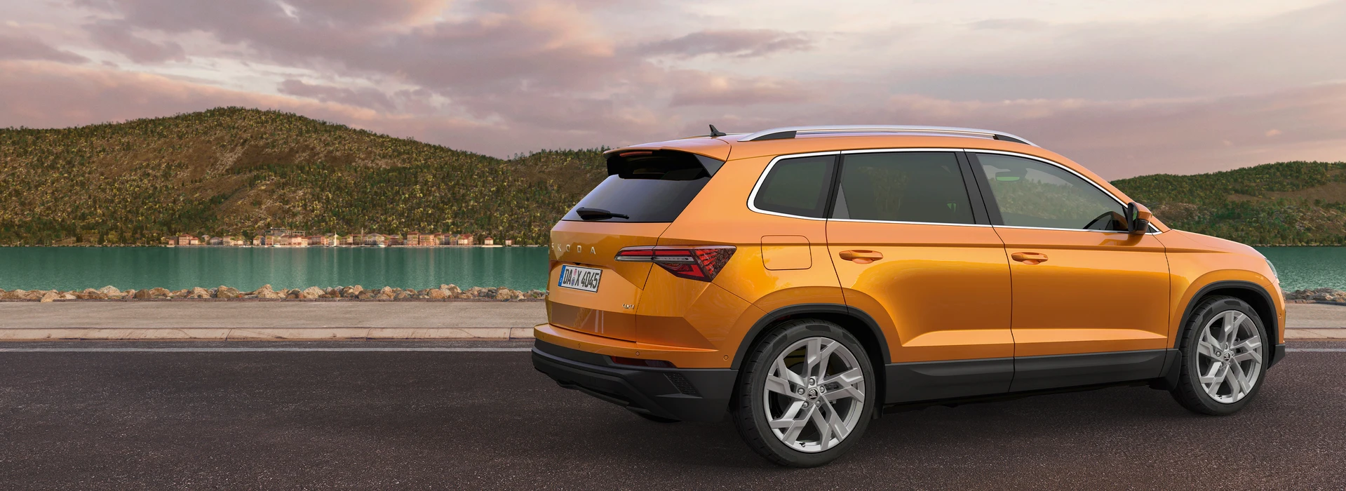 Škoda Karoq in Phoenix-Orange fährt die Straße entlang, ein See im Hintergrund