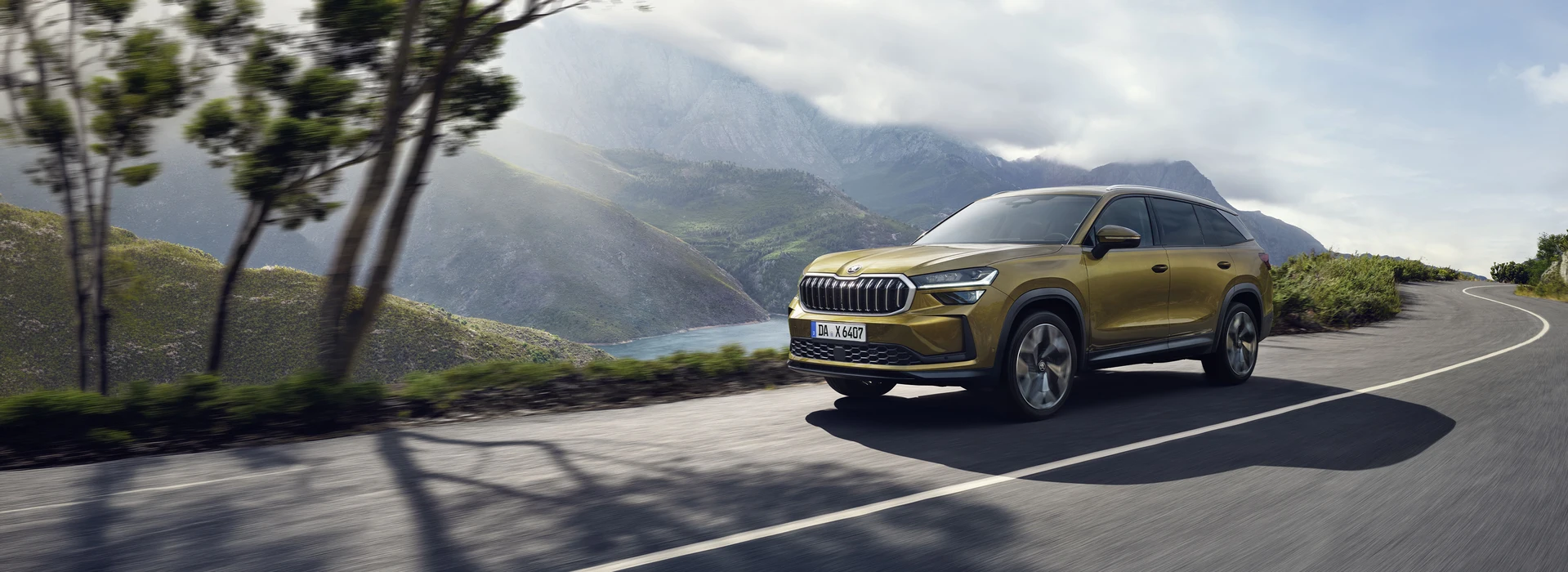 Goldfarbener Škoda Kodiaq fährt auf einer kurvigen Straße durch eine bergige Landschaft.