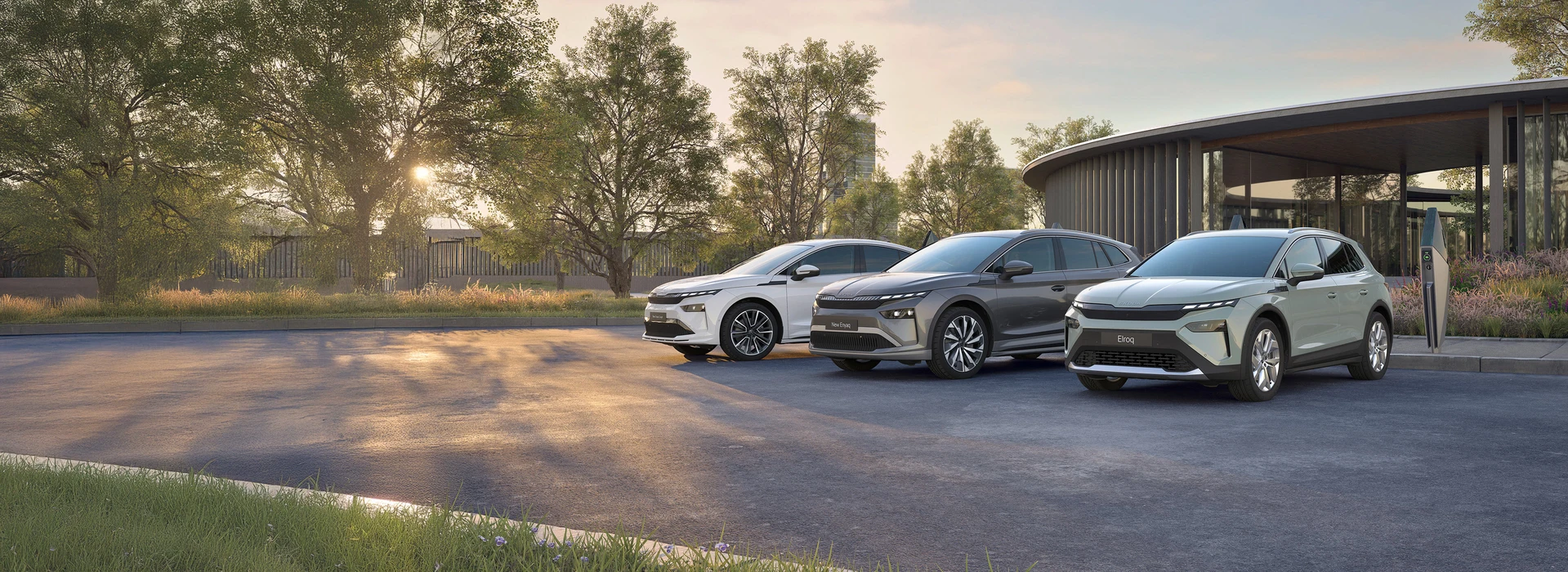Škoda Elroq, Enyaq und Enyaq Coupé stehen nebeneinander vor modernem Gebäude mit Bäumen.
