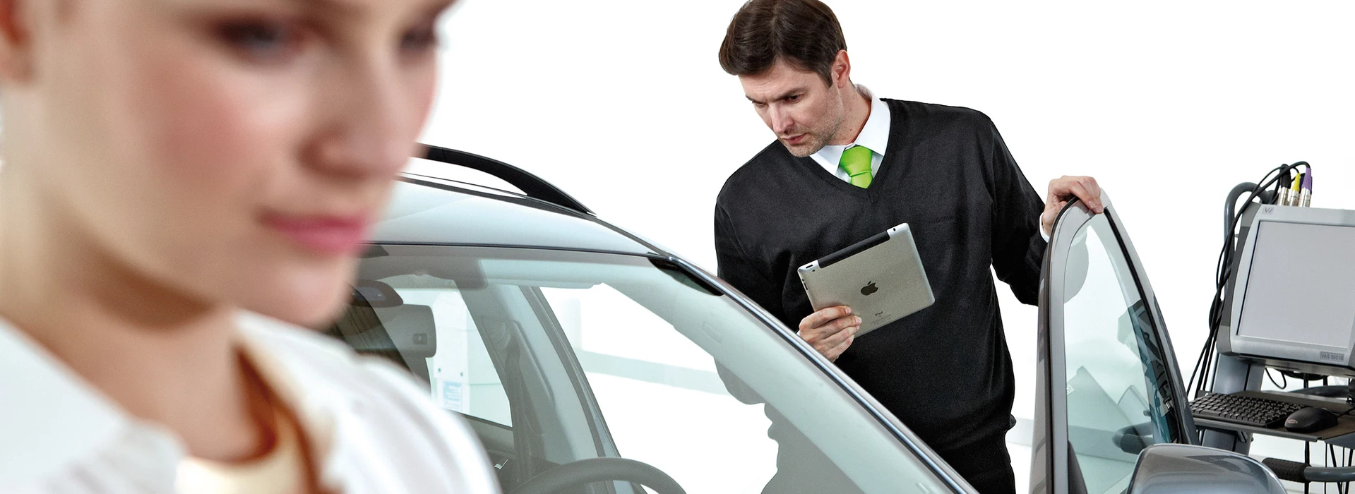 Berater inspiziert Fahrzeug mit Tablet vor Diagnosegeräten in heller Werkstatt