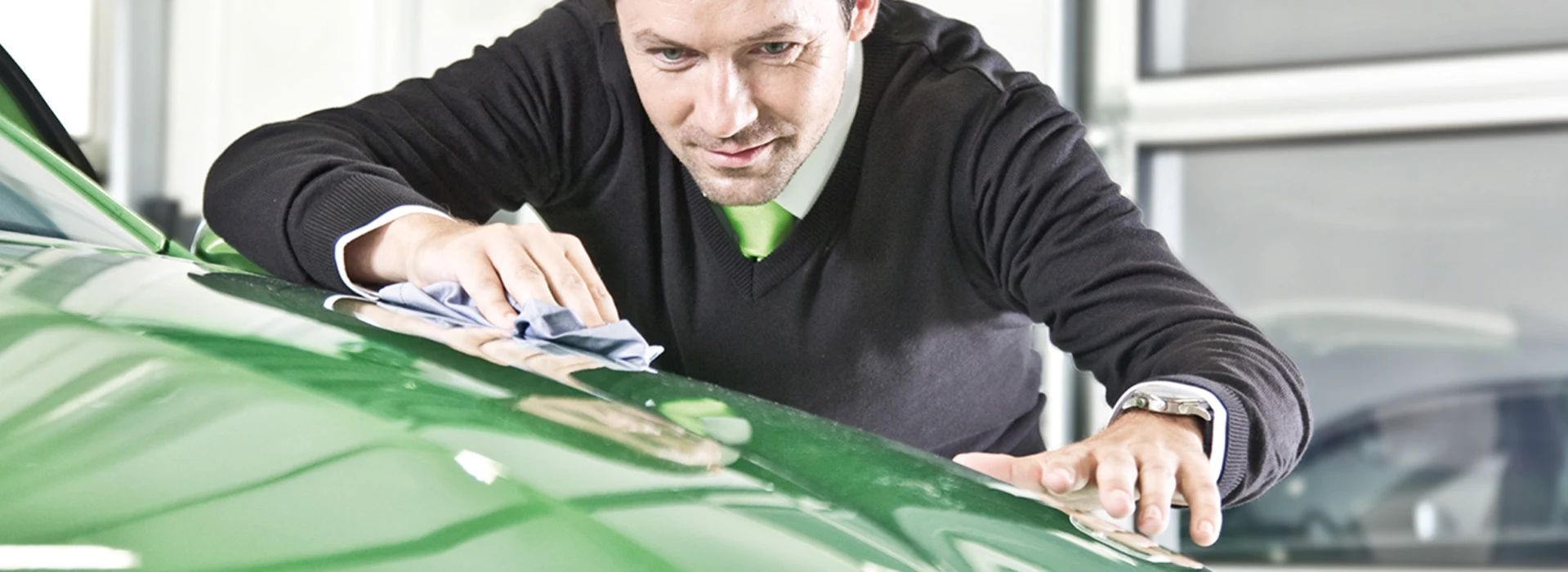 Ein Mann wischt sorgfältig ein grünes Auto ab, um ein Skoda-Garantieprogramm zu präsentieren.