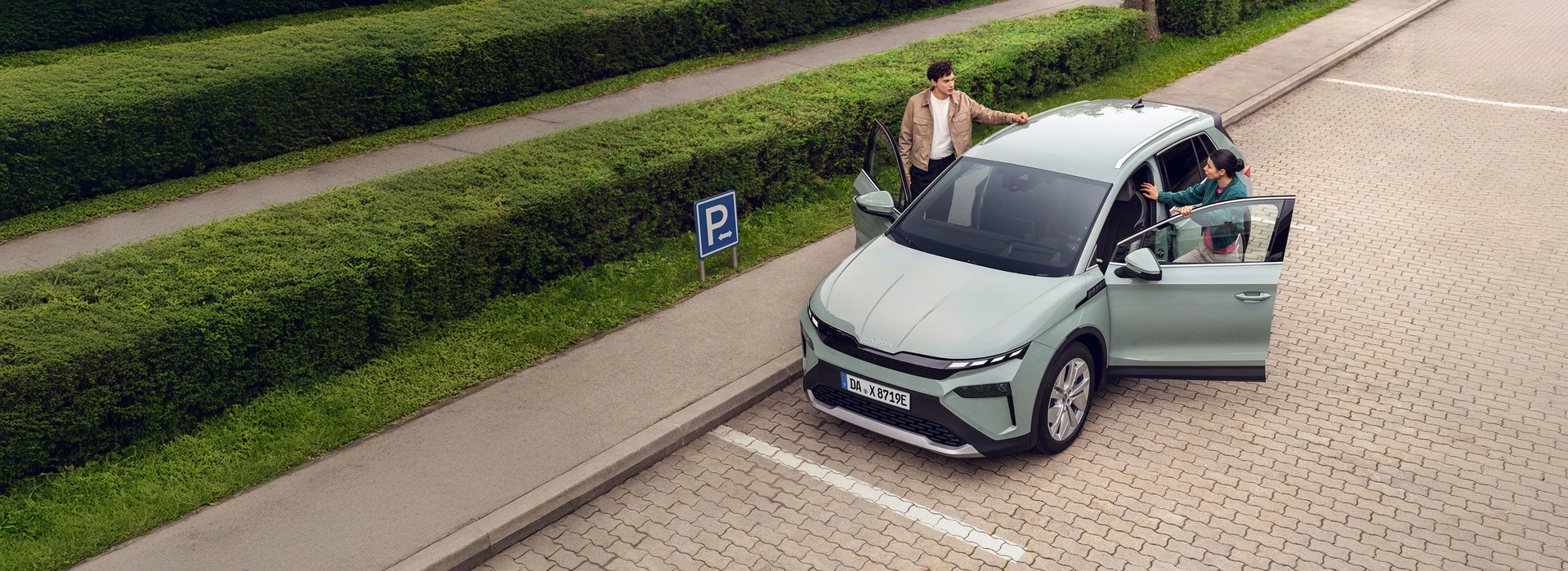 Paar steigt auf einem Parkplatz in einen mintgrünen Škoda Enyaq