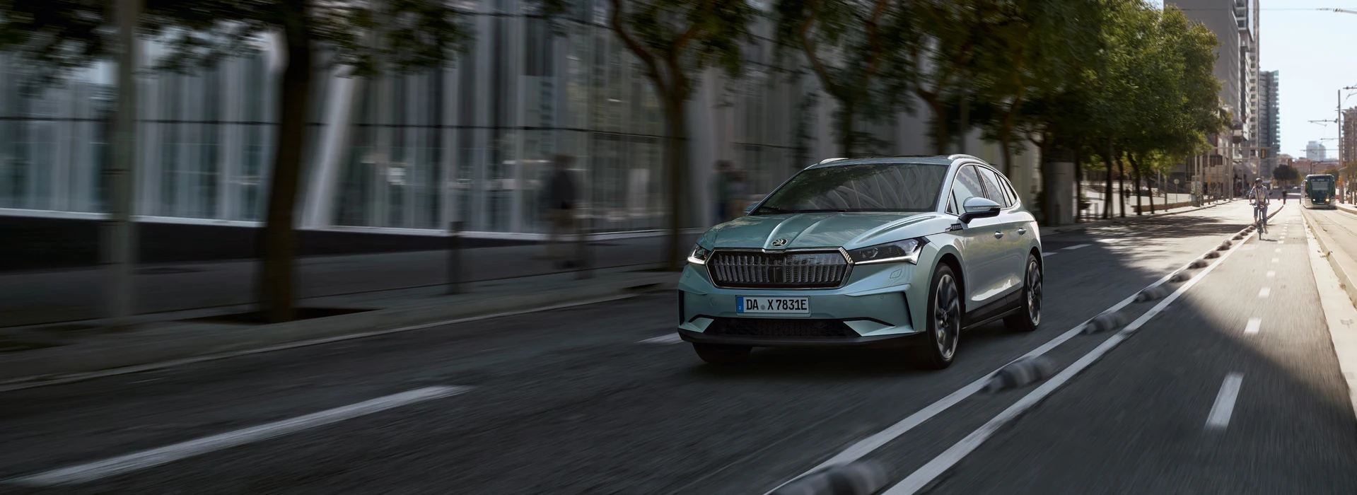 Škoda Enyaq fährt dynamisch durch eine moderne Stadt mit Radfahrer und Straßenbahn.