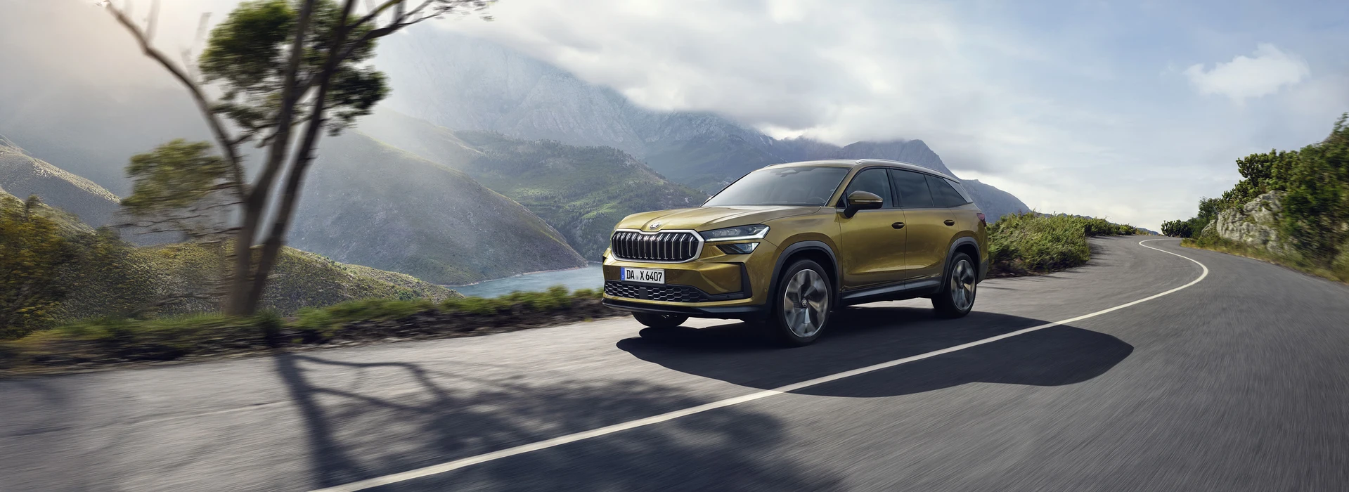 Škoda Kodiaq fährt auf einer kurvigen Küstenstraße durch bergige Landschaft mit Blick auf See und Natur.