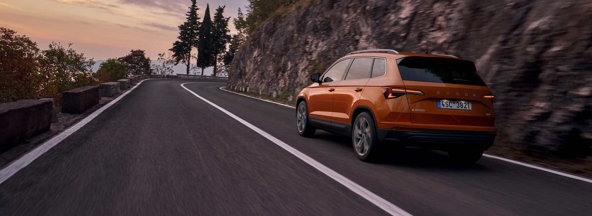 Škoda Karoq driving on the evening countryside road, ¾ rear angle, phoenix orange metallic color