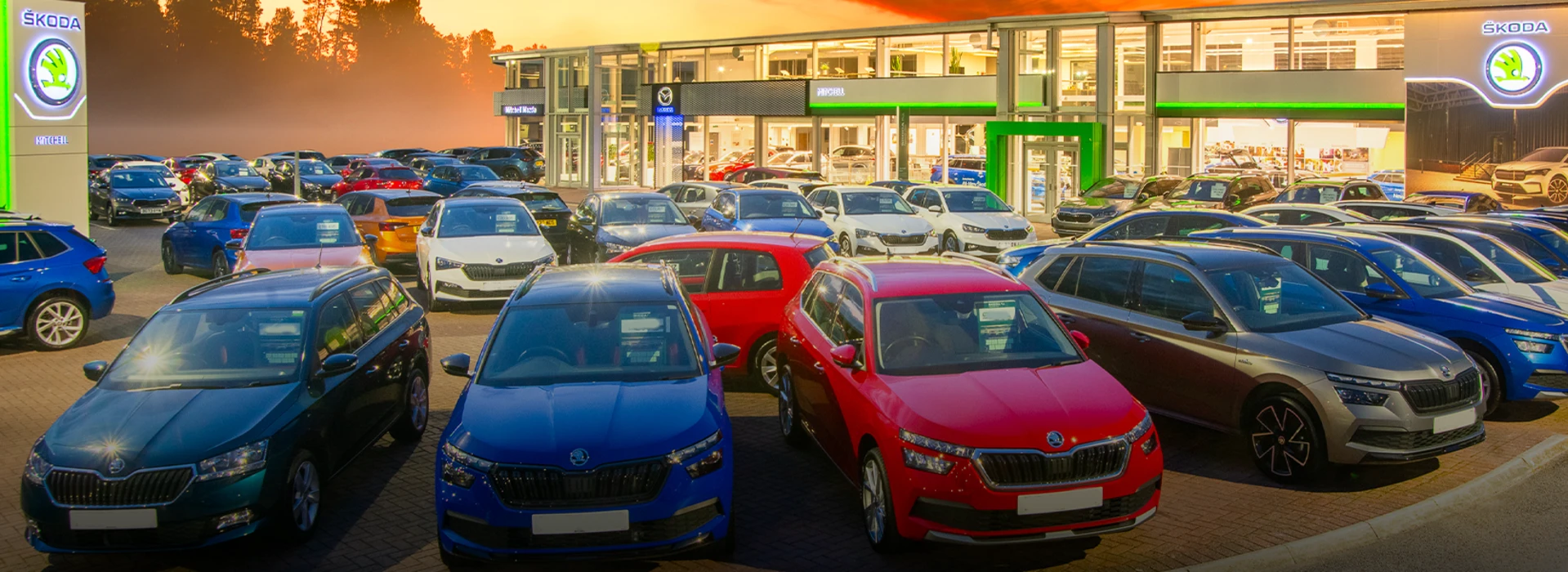 Škoda Mitchell Chester dealership forecourt packed with colourful parked cars at dusk.