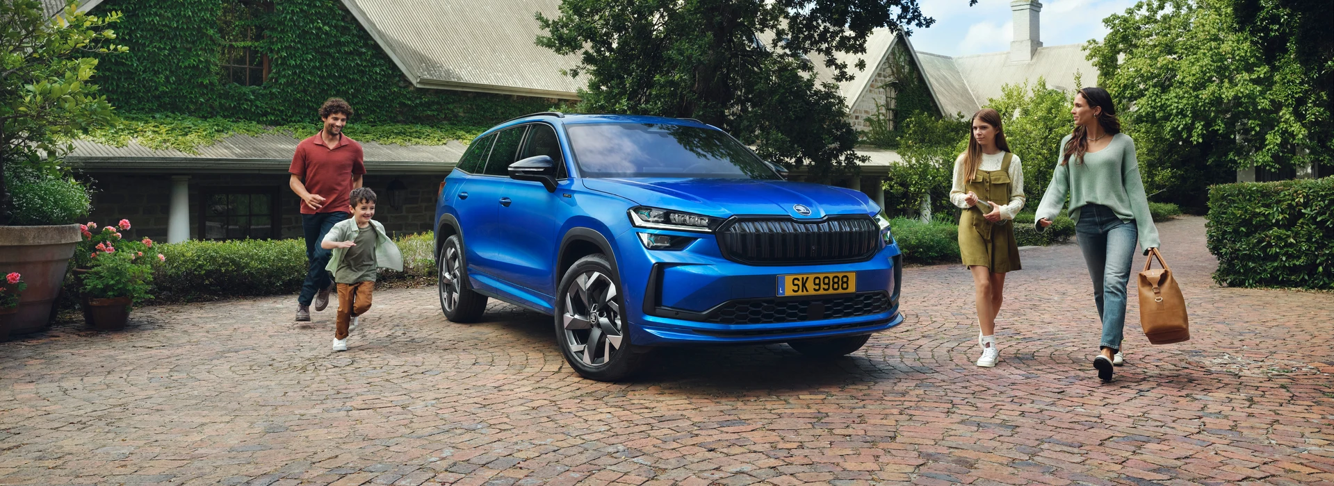 Gemini a dit Une famille de quatre personnes s'apprête à monter dans un SUV bleu électrique stationné dans l'allée pavée d'une grande propriété en pierre.