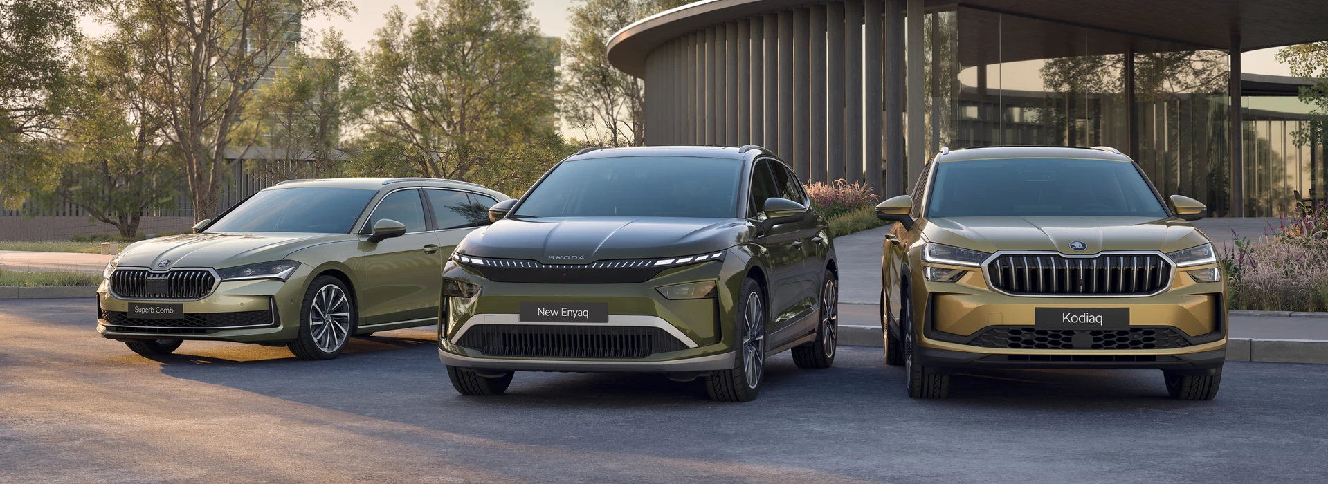 Une gamme de trois véhicules Skoda est garée devant un bâtiment moderne. On peut y voir la Superb Combi, la New Enyaq et la Kodiaq.