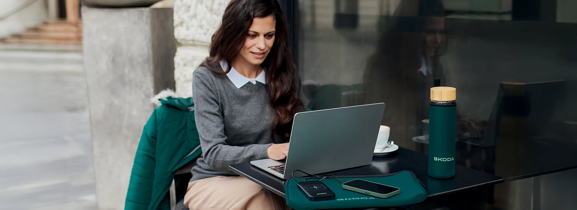 Une femme est assise devant un café et travaille sur son ordinateur portable.