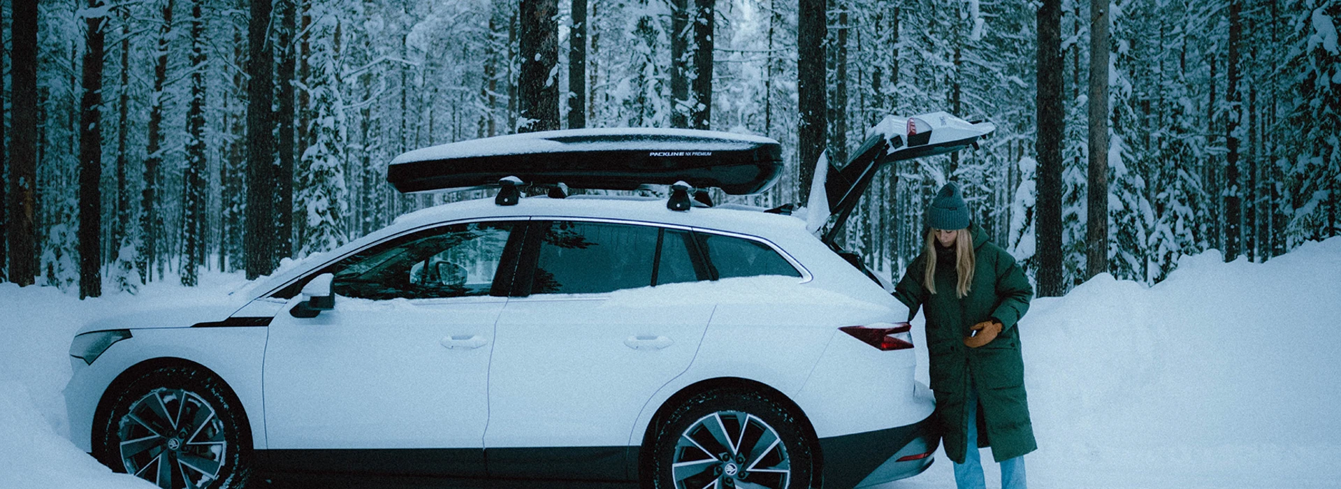 Škoda Enyaq i en vintrig, snöig skog med bakluckan öppen.