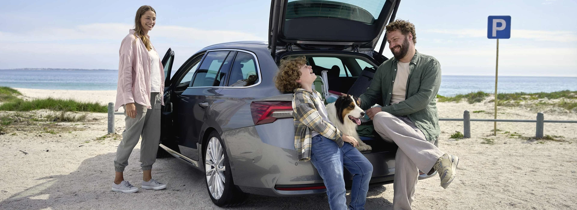 En familj med hund samlad runt en Skoda Octavia på stranden.