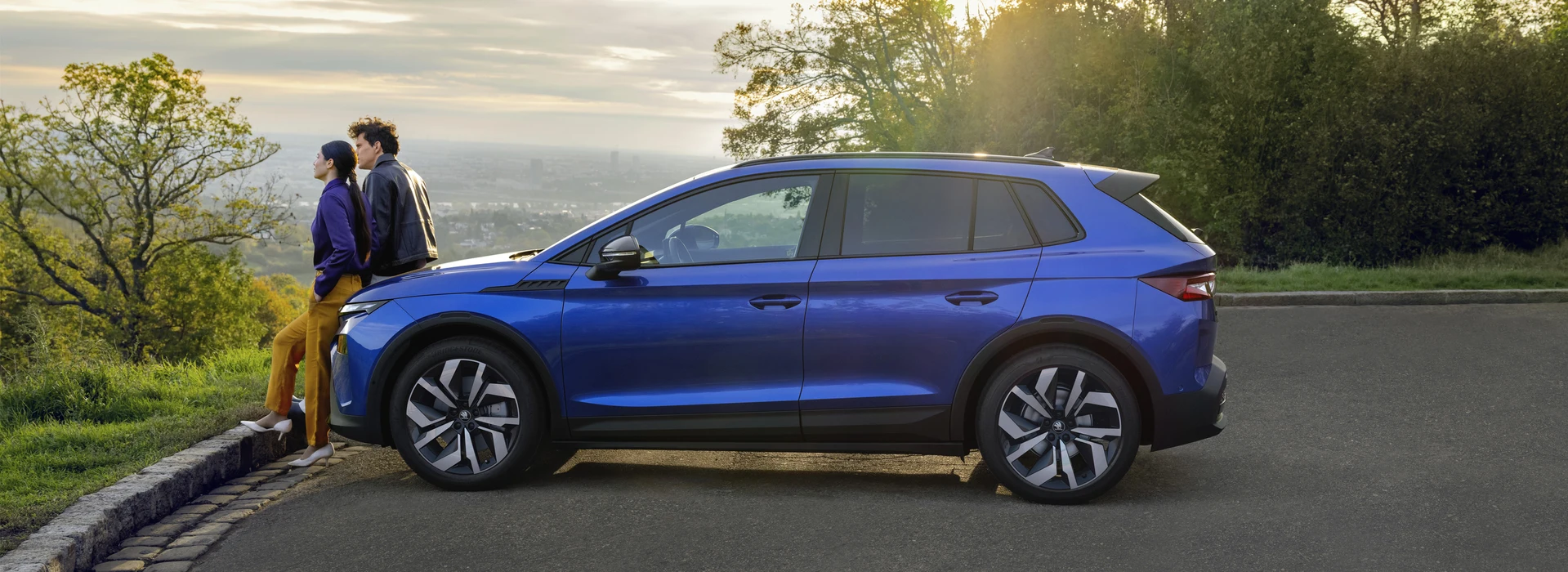 Två personer sitter på motorhuven på en Skoda Elroq och beundrar utsikten.