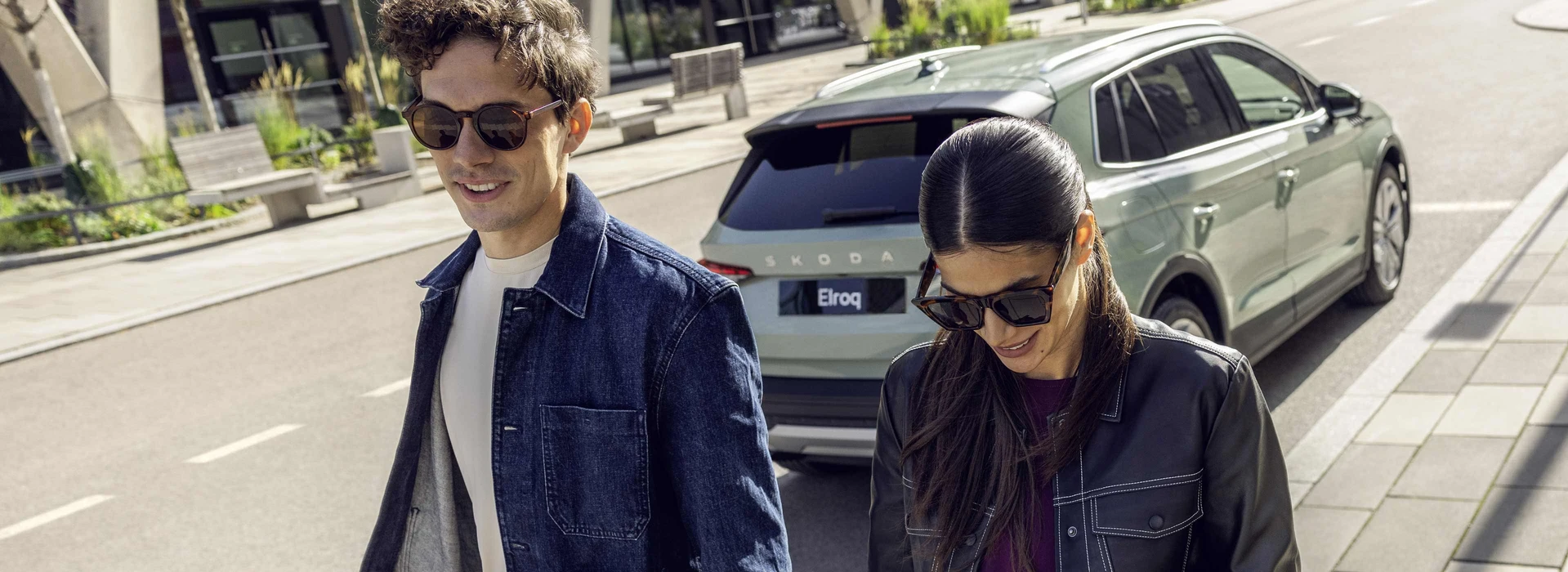 Två personer promenerar hand i hand förbi en Skoda Elroq elbil.
